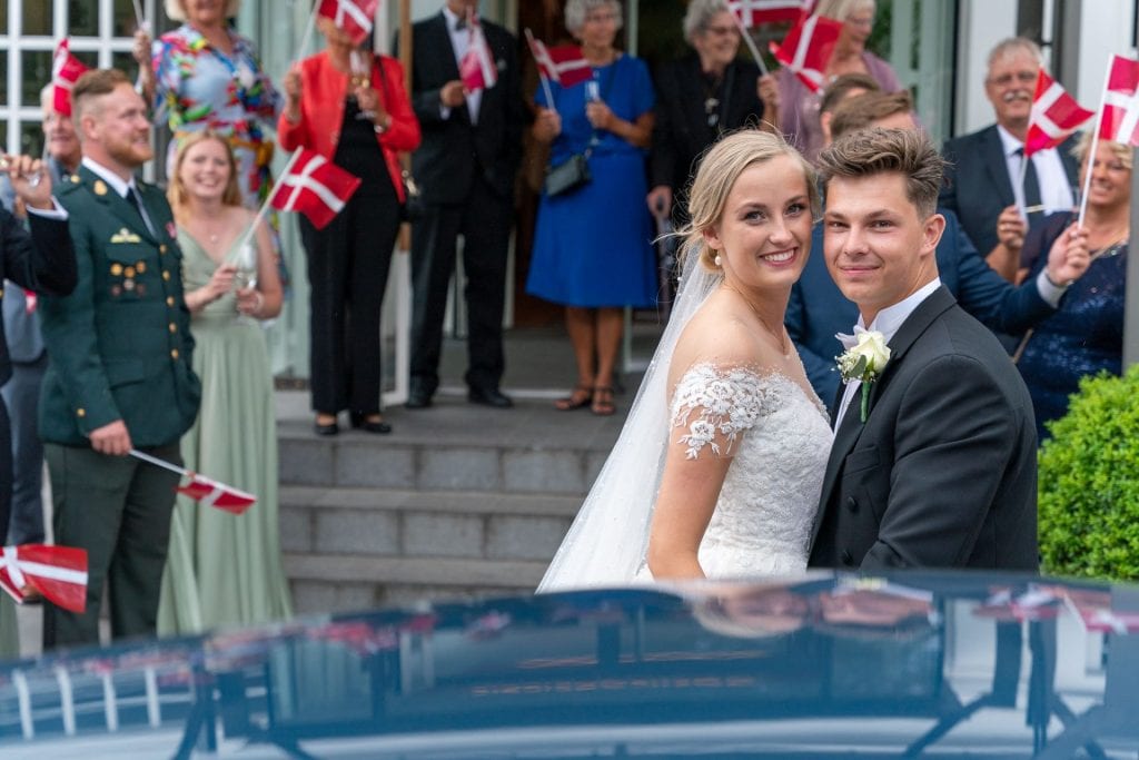 Brudepar foran festens gæster der vifter med dannebrog-flag